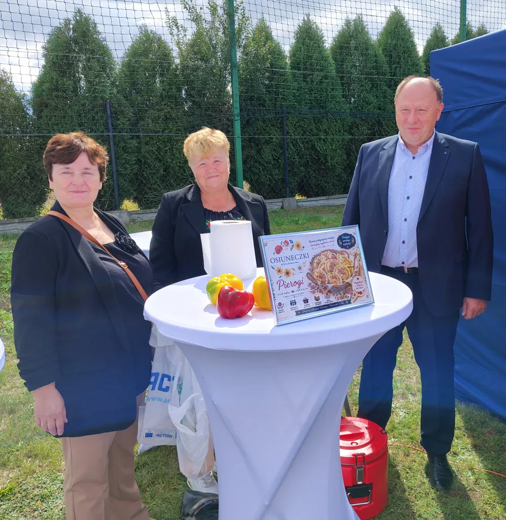 Uczestnicy pikniku przy stoliku z regionalnym wypiekiem i dekoracjami.