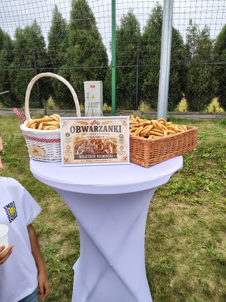 Kosze obwarzanków z tabliczką opisową na stoliku wystawowym.