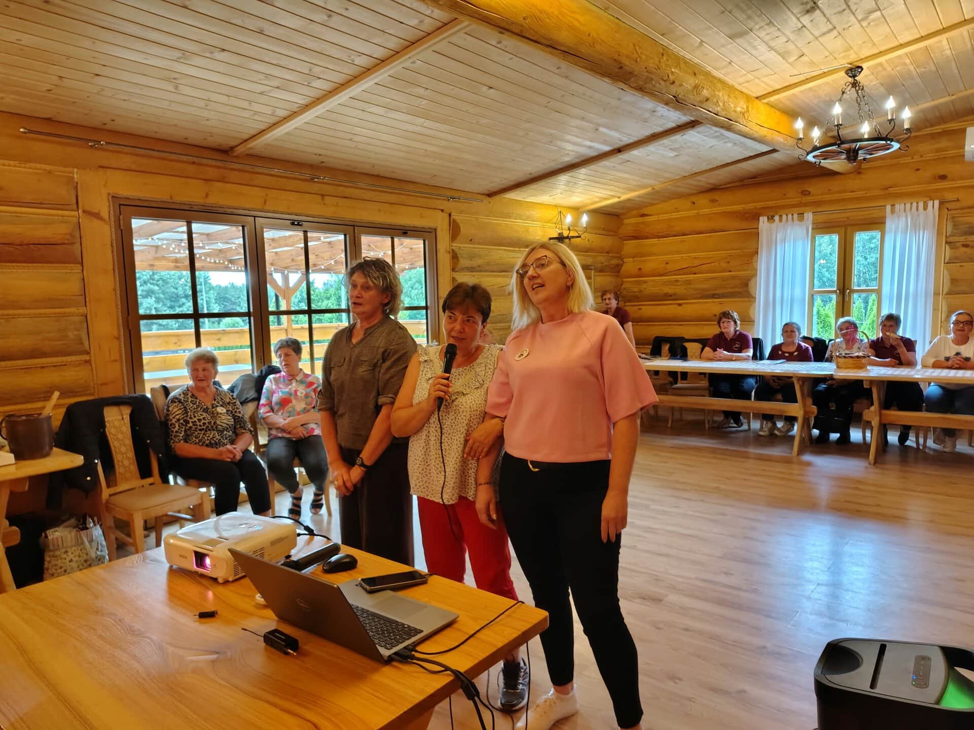 Uczestniczki karaoke śpiewają przy stoliku z laptopem i projektorem.