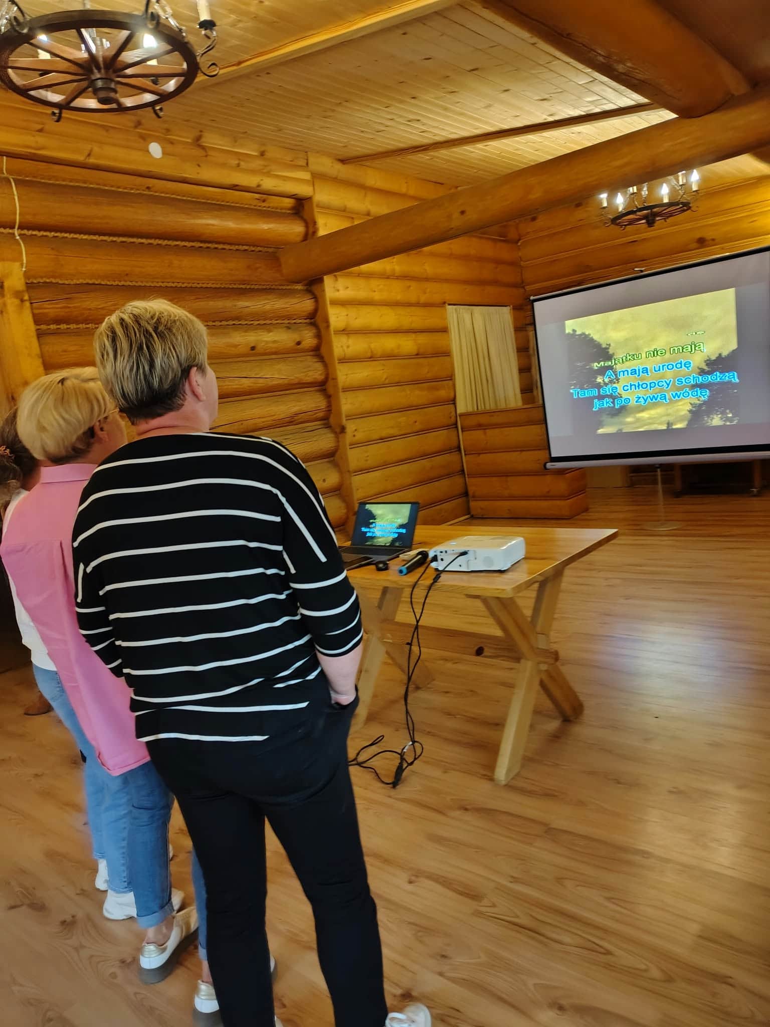 Uczestniczki karaoke odczytują słowa piosenki z ekranu projekcyjnego.